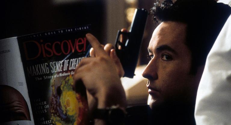 John Cusack holding a gun and reading.